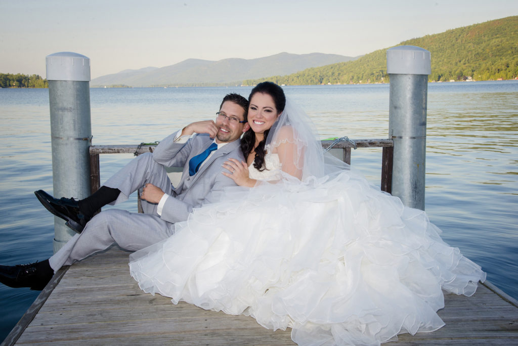 photographer bride and groom posing on dock by lake in mountains