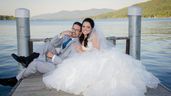 photographer bride and groom posing on dock by lake in mountains